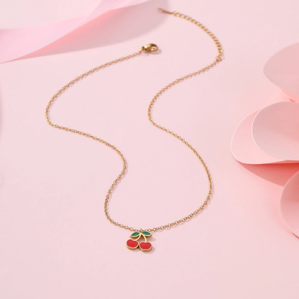 Four-piece cherry-themed jewellery set with gold electroplated necklace, bracelet, earrings, and ring on a white background.