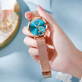 Rose gold alloy women's watch with mesh strap showing six dial colour options: white, black, blue, red, pink, and green.