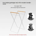 Black folding iron trash rack with a wooden handle holding a rubbish bag outdoors.