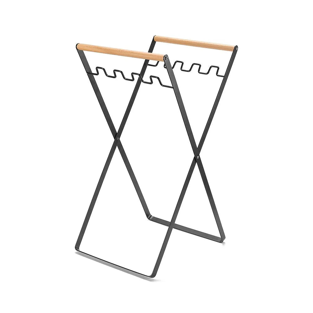 Black folding iron trash rack with a wooden handle holding a rubbish bag outdoors.