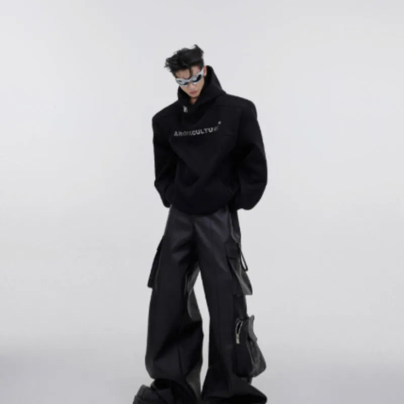 Man wearing a black loose-fit hooded sweater with heavy shoulder pads and a silver metallic graphic print on the chest.