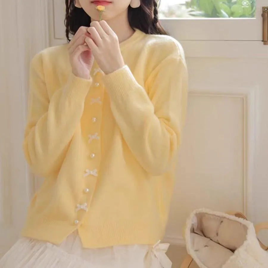 Women's cardigan sweater with a decorative bow and pearl buttons, shown in a solid colour.