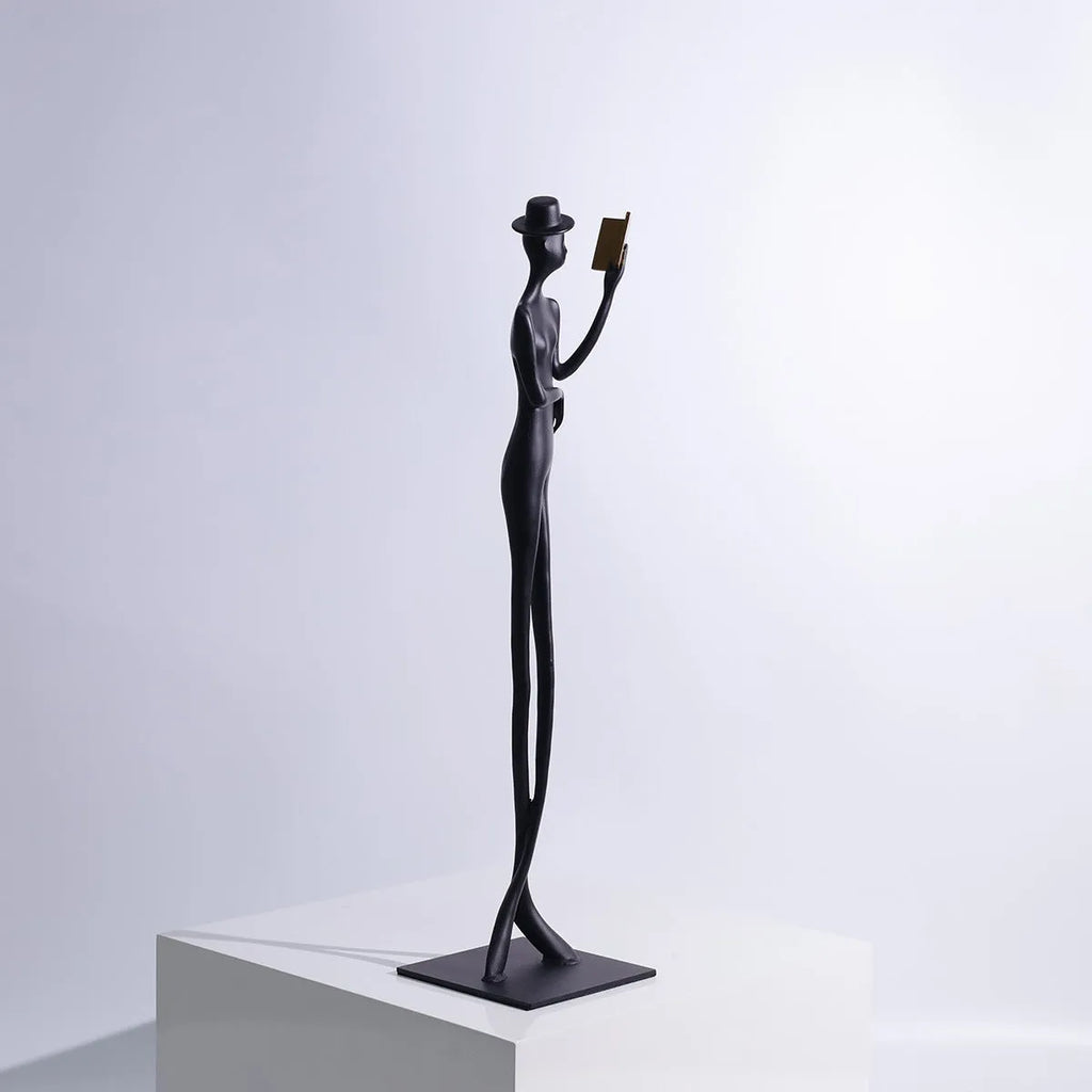 Black cast aluminium sculpture of a woman reading, 51cm tall on a desk.