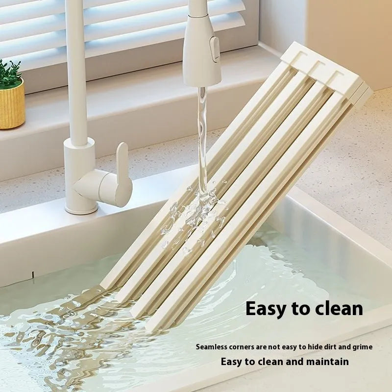 Foldable milky white stainless steel kitchen draining rack next to a sink.