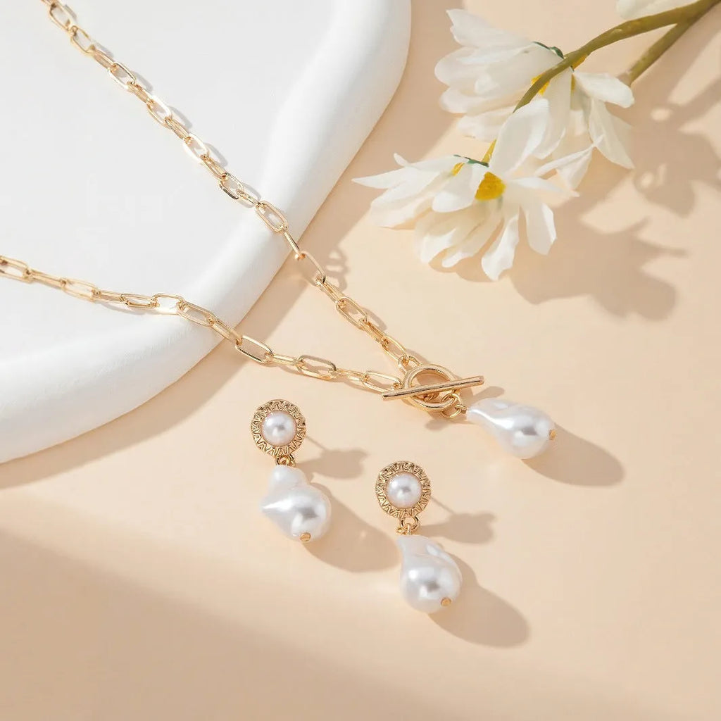 Gold retro baroque style necklace and earring set with pearl details on a white background.