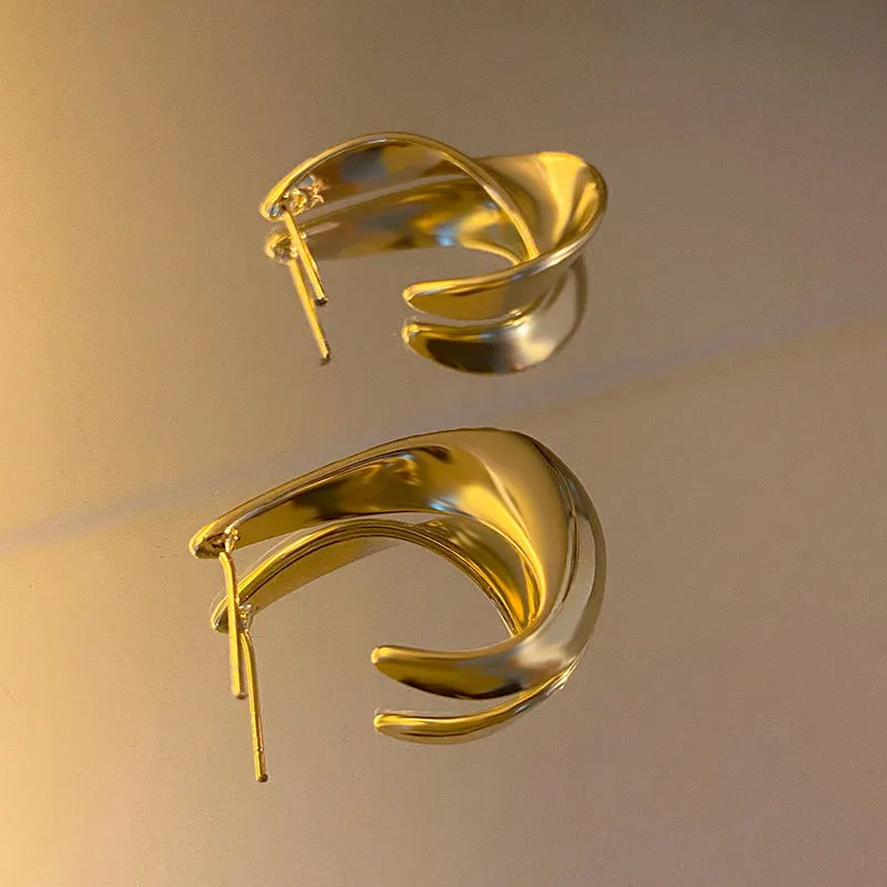 Close-up of gold twisted geometric metal earrings with a round design element.