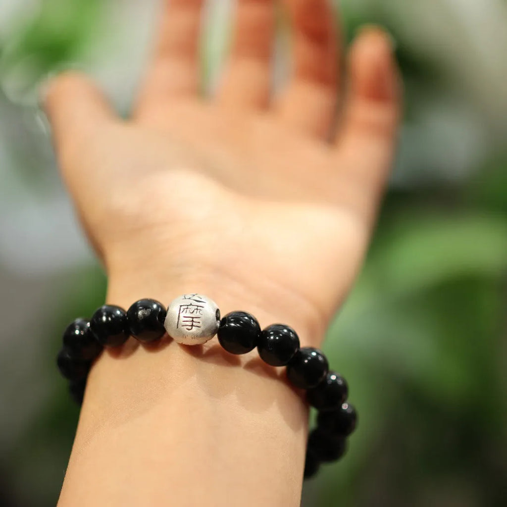Close-up of a bracelet with large round black agate beads and sterling silver components on a wrist.