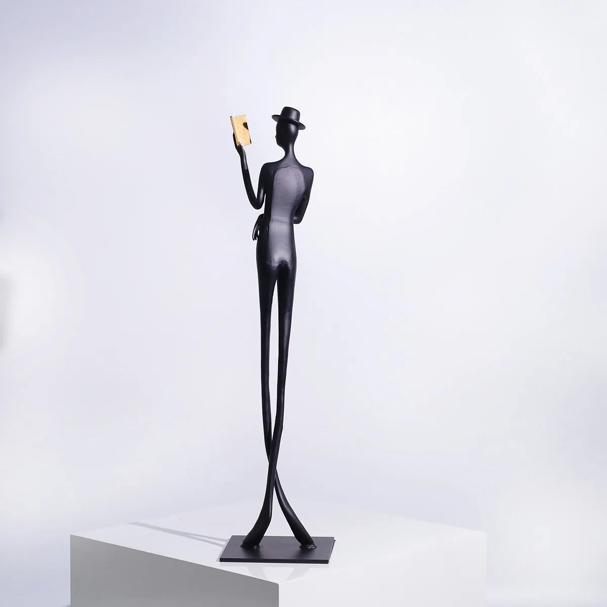 Black cast aluminium sculpture of a woman reading, 51cm tall on a desk.