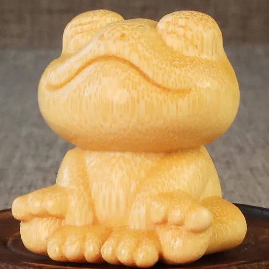 Solid bamboo smiling frog carving ornament with cartoon style on a wooden surface.