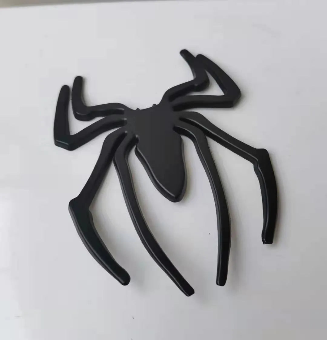 Three-dimensional metal spider bumper sticker in metallic finish on a car bumper.