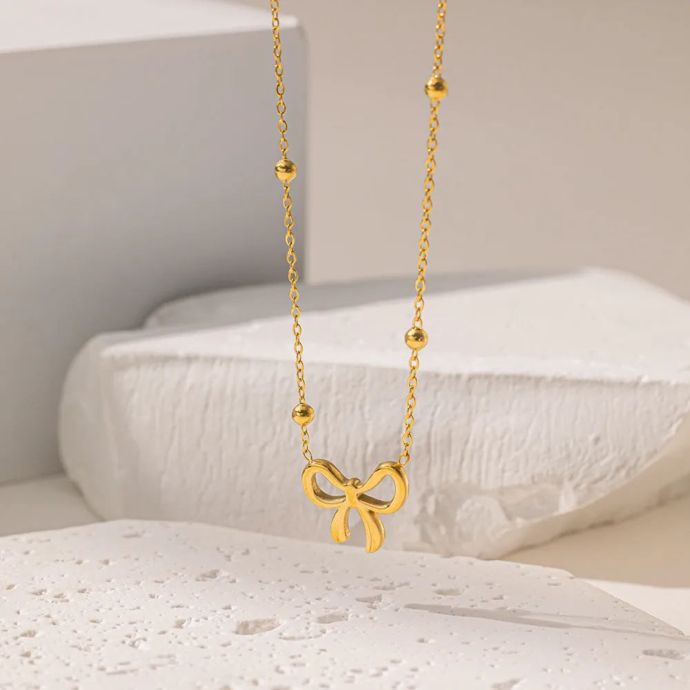 Gold-coloured titanium steel bow necklace with cross chain detail on white background