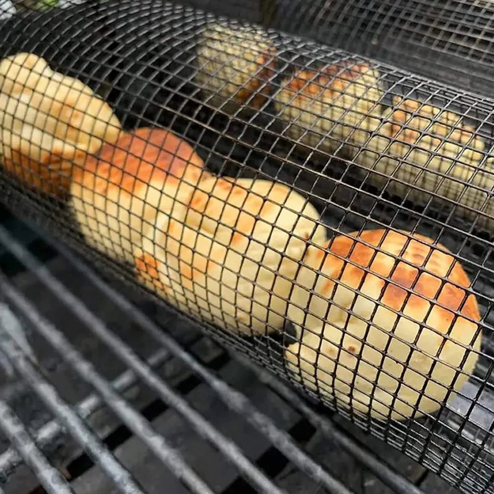 Rolling grill basket metal mesh cylinder with hooks on barbecue, containing vegetables and meat