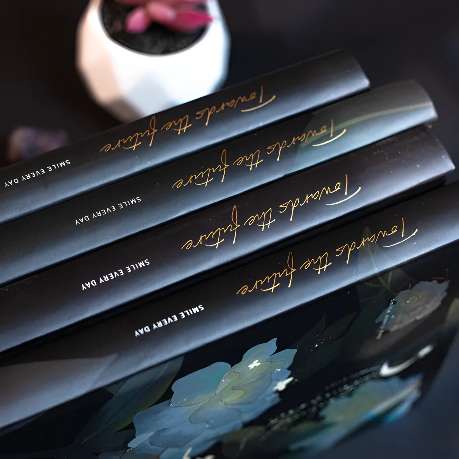 Four A5 hardcover notebooks with luminous covers in deep blue, gold, light blue, and purple colours.