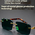 A pair of frameless dark green crystal sunglasses with a hard case and lens cloth.