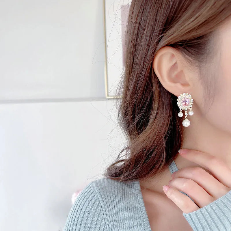 Oval geometric copper drop earrings with inlaid zircon stones, pearl details, and a tassel.