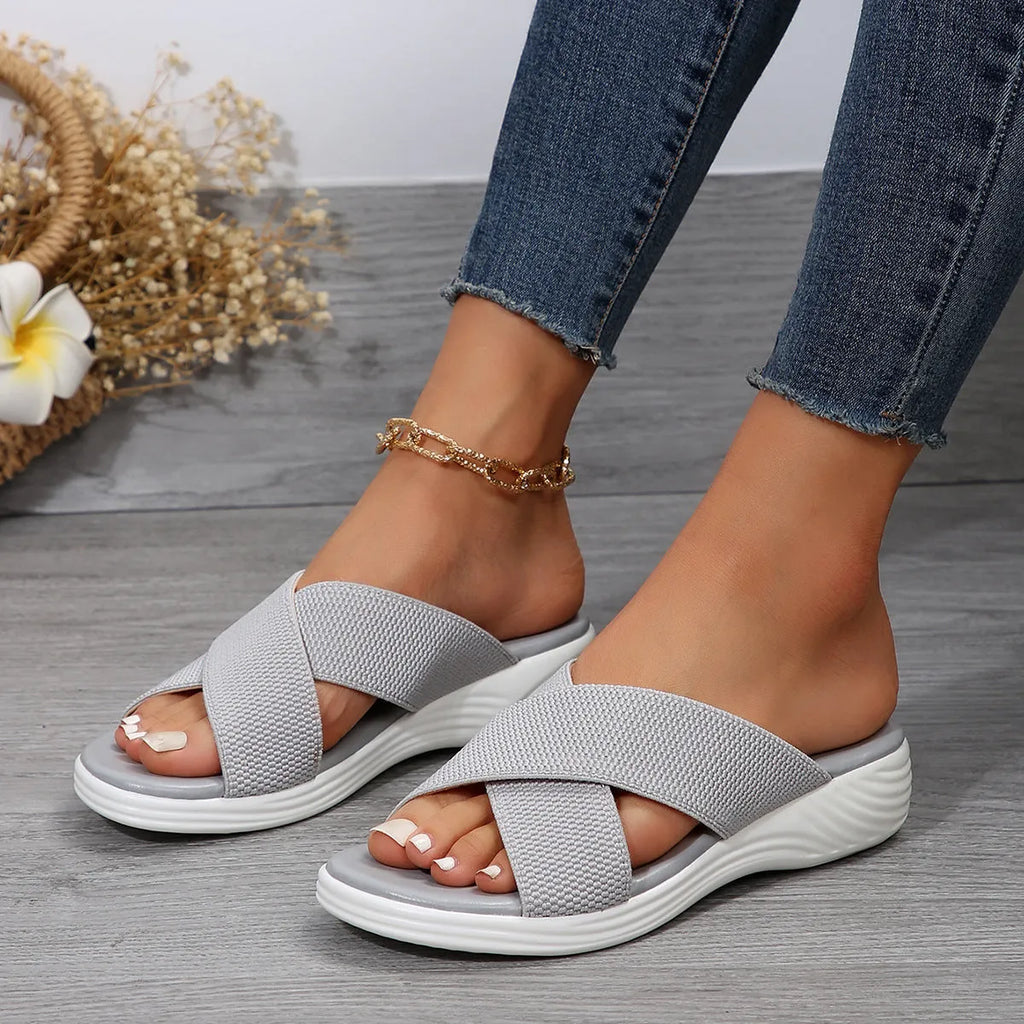 Black women's wedge slippers with cross-strap and thick rubber sole, showing peep-toe design