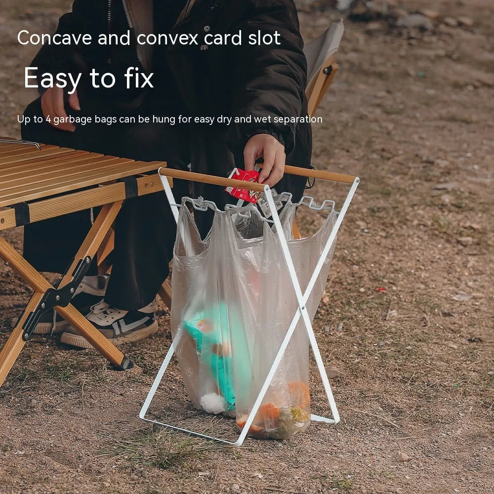 Black folding iron trash rack with a wooden handle holding a rubbish bag outdoors.